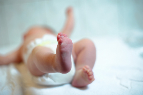 Close-up of a newborn baby lying on a soft surface in a diaper, with legs and tiny feet in focus.
