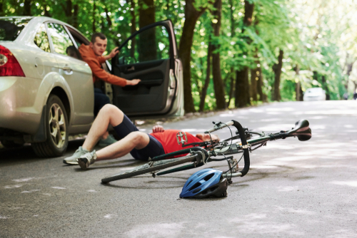 A cyclist lies on the ground after being hit by a car door suddenly opening, with the bicycle and helmet scattered on the road.