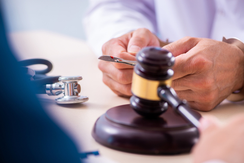 Close-up of a person holding a scalpel next to a judge&rsquo;s gavel and a stethoscope, symbolizing medical malpractice litigation.