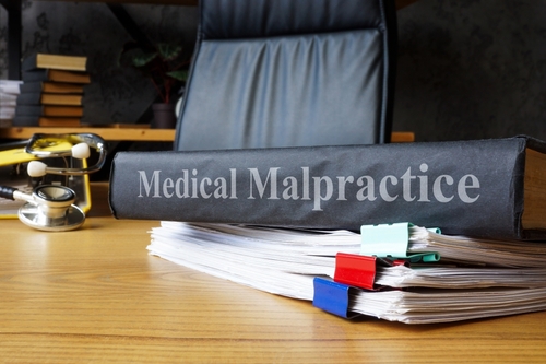 A binder labeled &ldquo;Medical Malpractice&rdquo; placed on a desk beside a large stack of documents with colored clips.