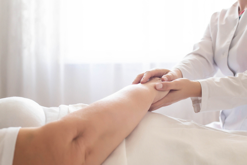 Doctor holding and examining the hand of a bedridden patient during a medical checkup.