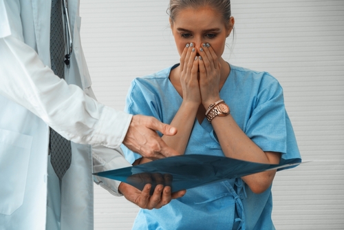 Concerned female patient covering her mouth while looking at medical scan results shown by a doctor.