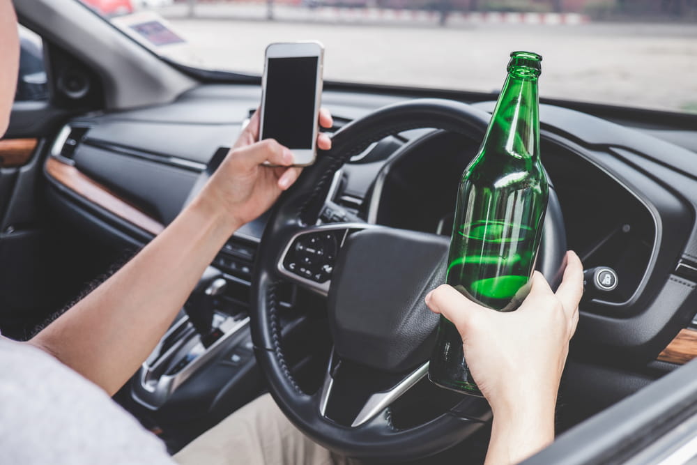 Driver holding a beer bottle and phone behind the wheel in Baltimore