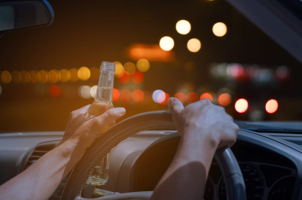 Driver holding a small liquor bottle while driving at night in Baltimore